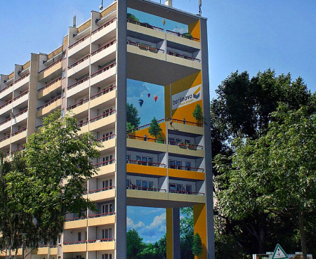 Eine großflächige Illusionsmalerin in Berlin an einem Hochhaus. Ein schönes Mural mit Balkonen und Landschaft, Personen und Tieren von Motiv–Wunsch.