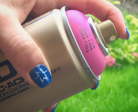 Eine Pinke Sprühdose von Montana Gold mit einer Hand, die Fingernägel sind mit dem Logo von Motiv-Wunsch bemalt.