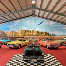 Ein Landschaftsmotiv mit der Route 66 in einem Showroom, davor Oldtimer. Die von Motiv-Wunsch gestaltete Halle ist in Teltow.