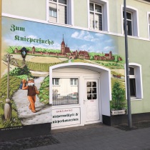 Aussenfassade mit einer historischen Ansicht mit Bezug auf das Ladengeschäft. Werbemalerei von Motiv-Wunsch in Pritzwalk.